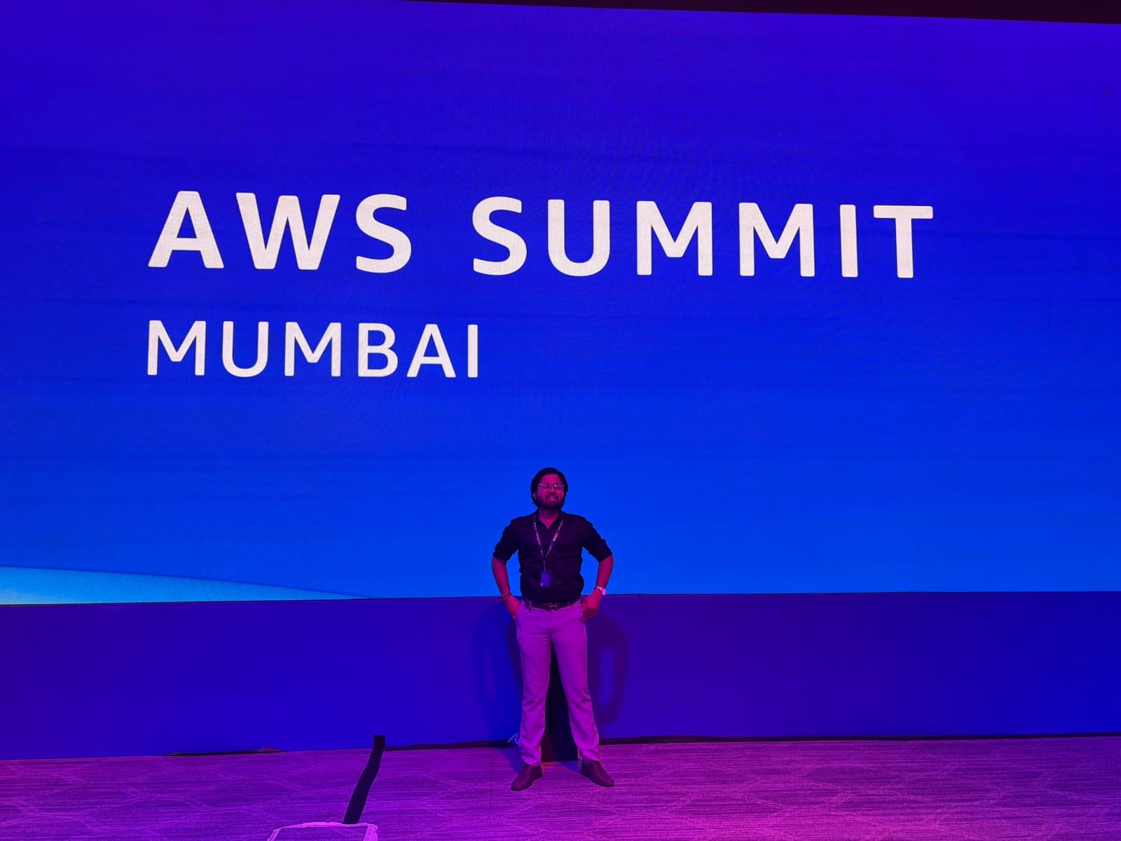 Ankit Vala standing in front of the AWS Summit Mumbai stage screen at the conference.