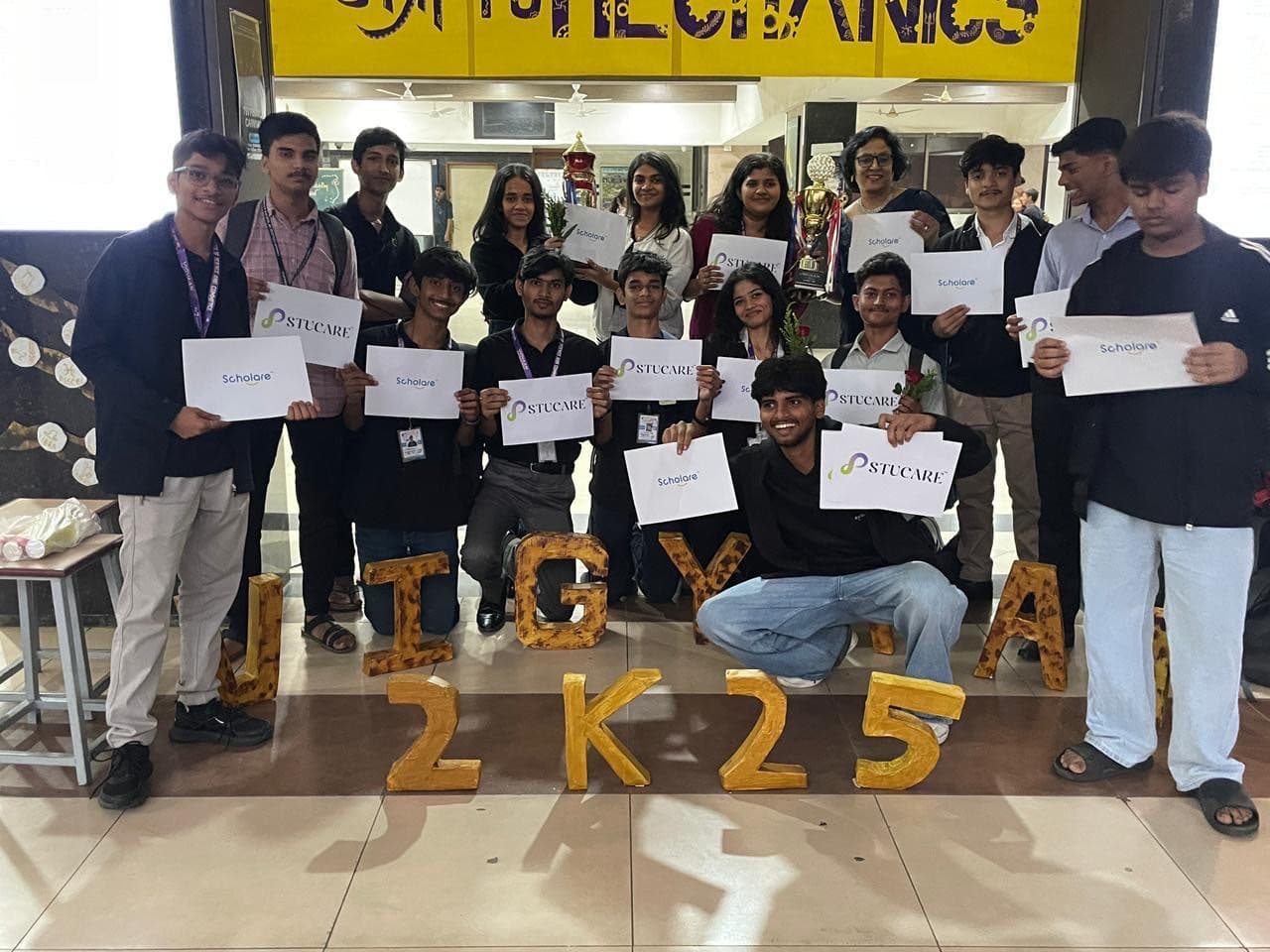 A group of students holding Scholare and Stucare cards at JTGYA 2K25, below the Mechanics department banner